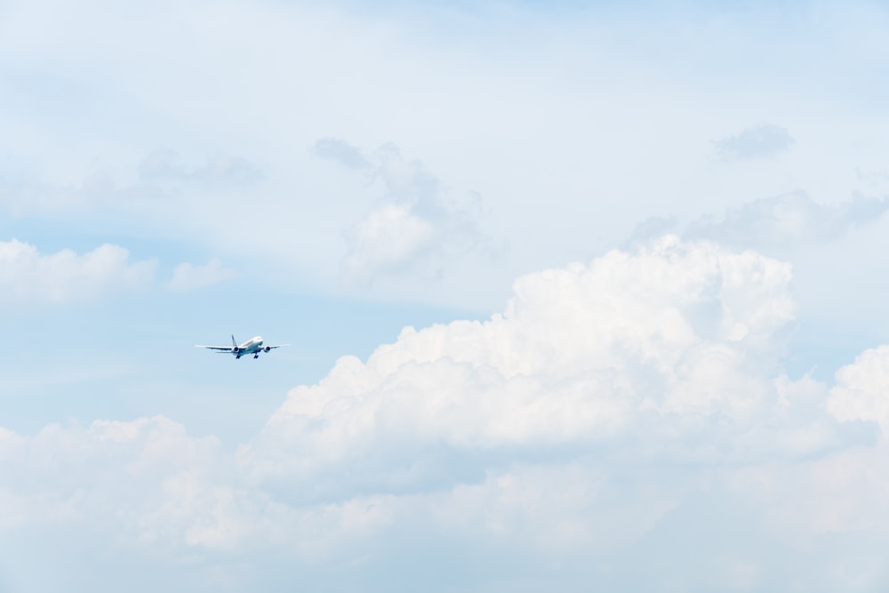 白い雲の下を飛ぶ白い民間飛行機の写真
