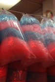 Several bags containing colorful cotton candy hang from a string. The cotton candy is pink and blue, creating a fluffy and light texture inside clear plastic bags.