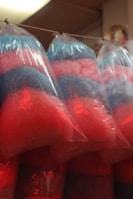 Several bags containing colorful cotton candy hang from a string. The cotton candy is pink and blue, creating a fluffy and light texture inside clear plastic bags.