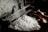 A pair of hands is working with a tool to unravel silk threads from white silkworm cocoons placed in steaming hot water. The industrial setup seems rustic, highlighting the traditional method of silk production.