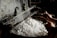 A pair of hands is working with a tool to unravel silk threads from white silkworm cocoons placed in steaming hot water. The industrial setup seems rustic, highlighting the traditional method of silk production.