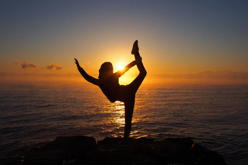 A man over 40 doing yoga on a mountain overlook at sunrise