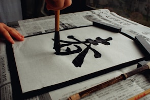 A neatly handwritten kanji character on traditional Japanese paper with a brush pen beside it.