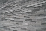 An extensive wall made of stacked, elongated stone tiles arranged in a staggered pattern. The tiles vary slightly in shade, creating a textured and layered appearance.