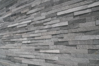 An extensive wall made of stacked, elongated stone tiles arranged in a staggered pattern. The tiles vary slightly in shade, creating a textured and layered appearance.