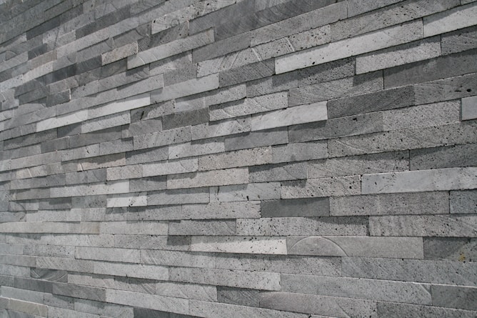An extensive wall made of stacked, elongated stone tiles arranged in a staggered pattern. The tiles vary slightly in shade, creating a textured and layered appearance.