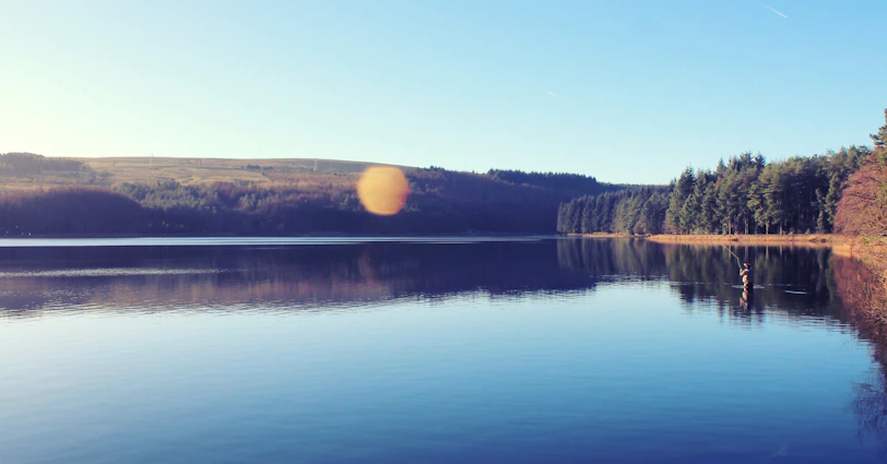 Peaceful lake view with reflections and a player casting a line in the game.