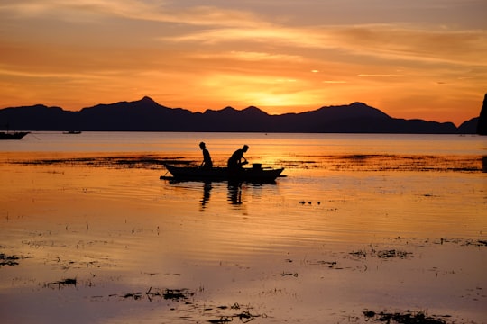 silhouette of two people riding boat on body of water during golden hour in Corong Corong Beach Philippines