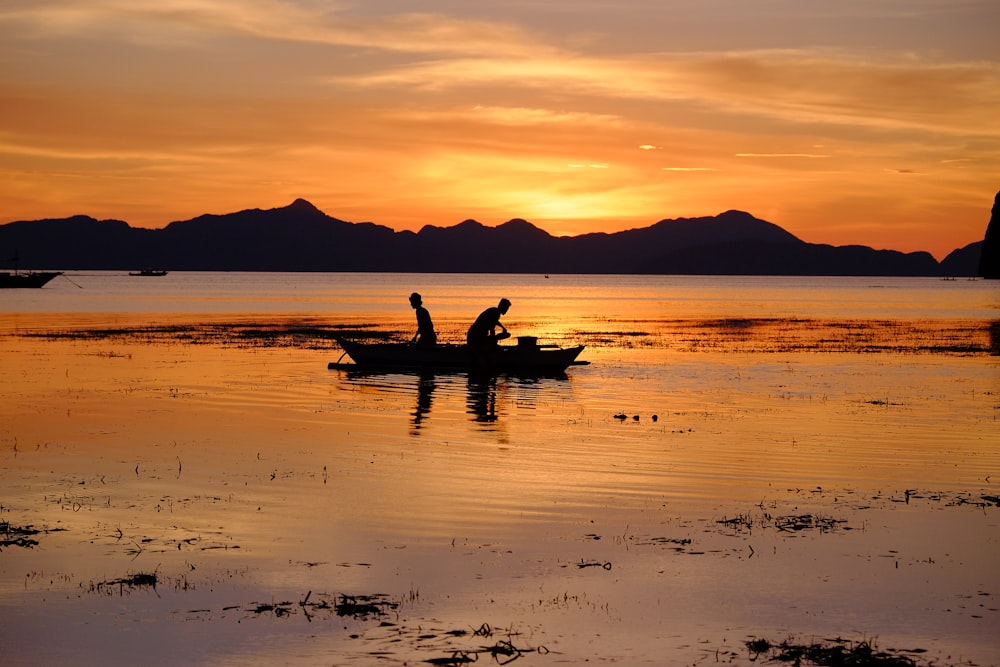 silhouette of two people riding boat on body of water during golden hour