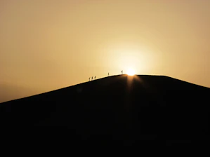 A group of travelers trekking across golden desert dunes at sunset.