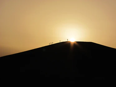 A group of travelers trekking across golden desert dunes at sunset.