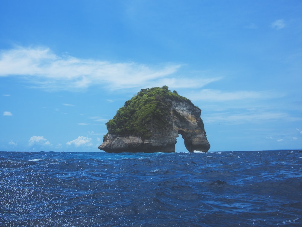 isla de roca arqueada bajo cielo nublado azul y blanco