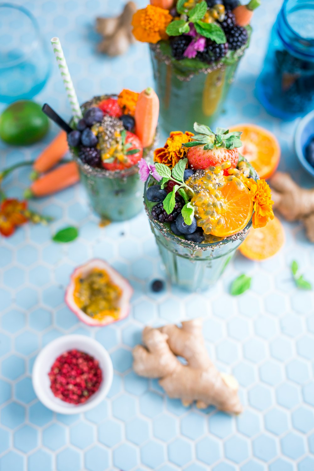 Fruit smoothies in glasses topped with pieces of fruit and marigold flowers