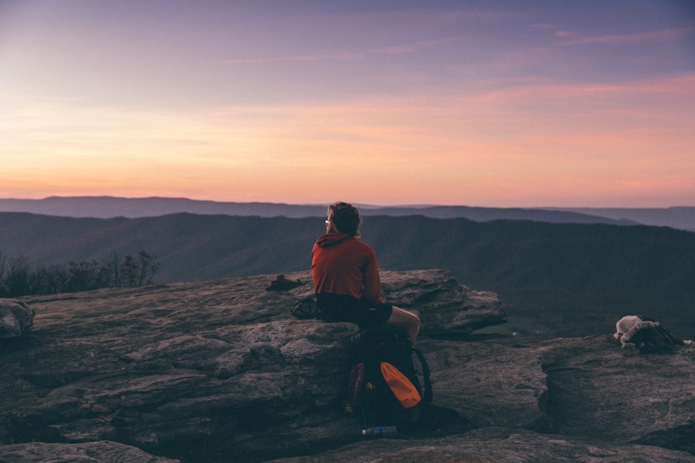 person sitting on boulder overlooking mountain during golden hour