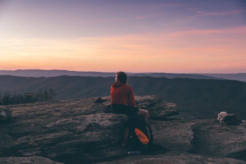 Hiker sitting on a rock outcrop overlooking a mountain ridge