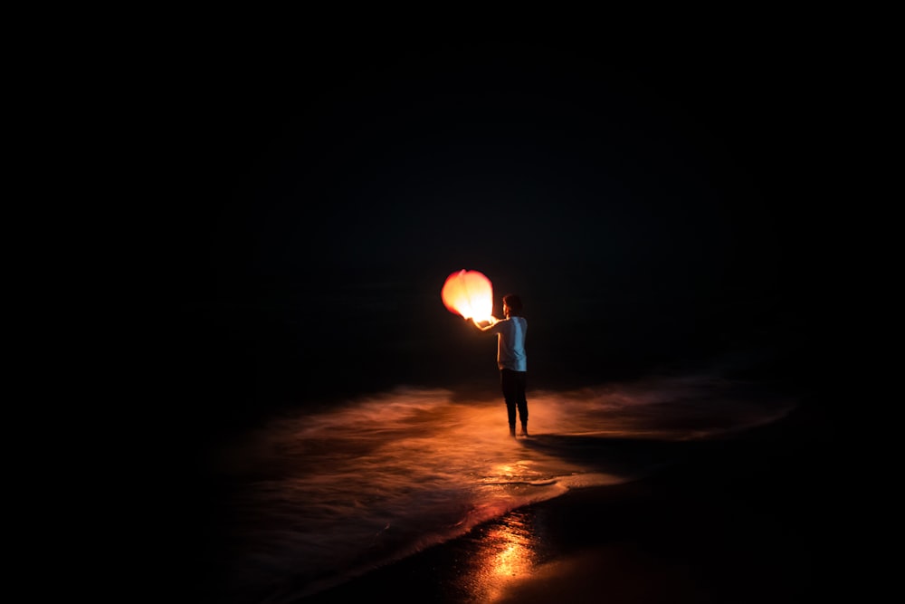 person standing on shore holding brown paper lantern