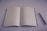 A blank, open notebook is placed on a smooth surface next to a pen. The background and the notebook pages are predominantly white, creating a minimalistic look.