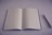 A blank, open notebook is placed on a smooth surface next to a pen. The background and the notebook pages are predominantly white, creating a minimalistic look.