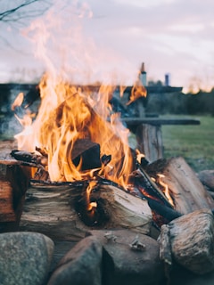 Close-up of a campfire glowing warmly as dusk falls, surrounded by smooth stones and soft grass