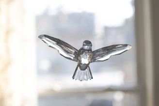 A crystal sculpture of a bird with outstretched wings, set against a softly blurred background. The intricate facets of the crystal play with the light, creating reflections and highlighting the bird's detailed design.