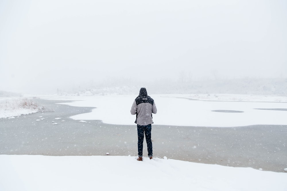 man standing on snow field facing river
