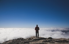 man standing on brown mountains facing sea of clouds
