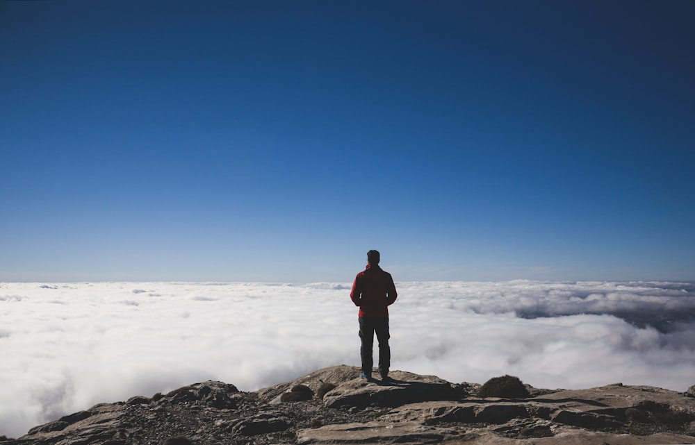 homem de pé em montanhas marrons de frente para o mar de nuvens
