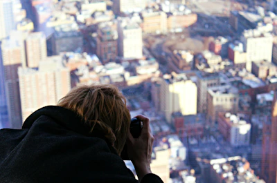 An urban travel scene showing a male creator capturing cityscapes from a rooftop viewpoint.