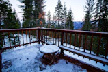 Spacious balcony overlooking snow-covered pine trees at sunset.