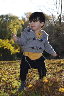 A child wearing a Ludora jacket, exploring a leafy backyard on a crisp day.