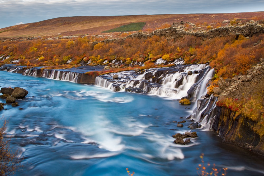 Landschaftsfotografie von Wasserfällen, die von braunen Feldern umgeben sind