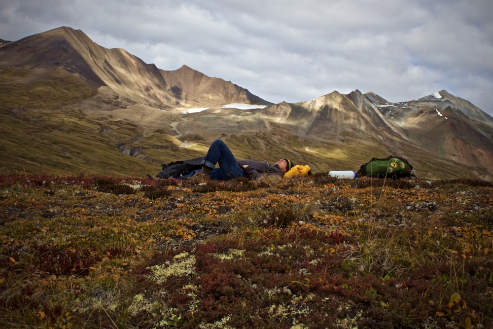 man lying on plant field near mountains