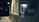 A close-up view of an outdoor electric meter mounted on a wall. The background is dimly lit, indicating it might be nighttime. The area surrounding the meter is illuminated by artificial light, creating a contrast between the bright and dark areas.