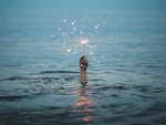 person submerged on body of water holding sparkler