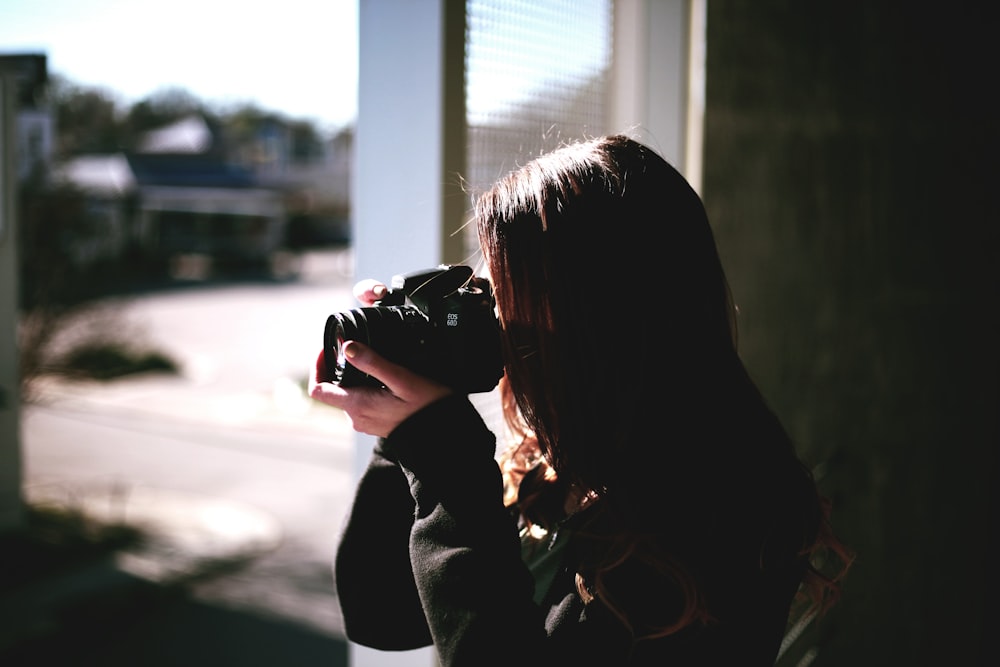 femme tenant un appareil photo reflex numérique noir