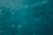 An underwater view with a hazy, bluish-green hue. The image captures the motion and fluidity of water, with small bubbles or particles visible throughout.