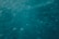 An underwater view with a hazy, bluish-green hue. The image captures the motion and fluidity of water, with small bubbles or particles visible throughout.