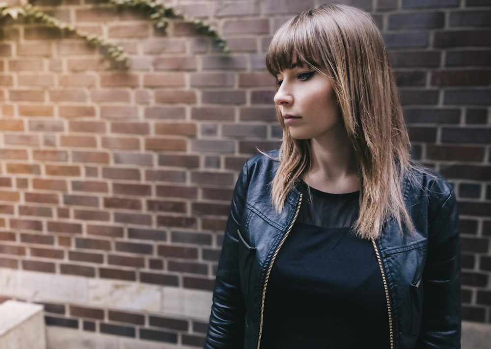 コンクリートのレンガの壁のそばに立つ黒いジャケットを着た女性