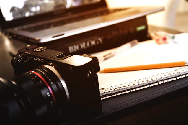 A candid shot of a camera resting on a wooden table beside a notebook filled with handwritten notes.