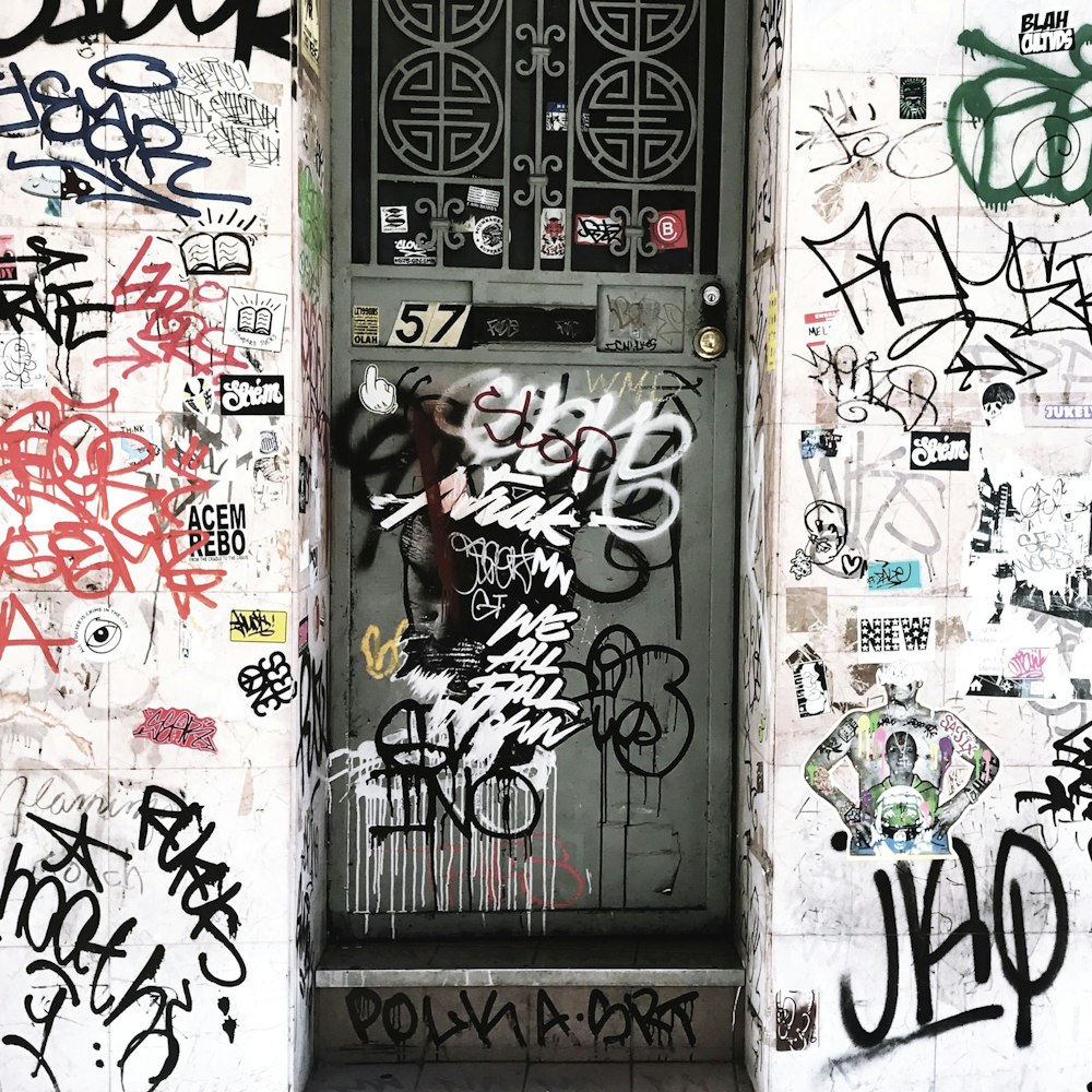 a door covered in lots of graffiti next to a wall