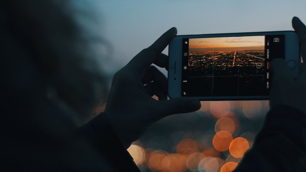 person capturing photo of city using iPhone during orange sunset