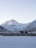 A majestic snow-covered mountain range with a prominent peak under a clear sky. The foreground features grazing yaks on a rocky, snow-dusted plain.