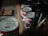 A collection of old and used paint cans is lined up on a wooden surface, accompanied by several paintbrushes in a container. The setup suggests a workspace for painting or DIY projects.