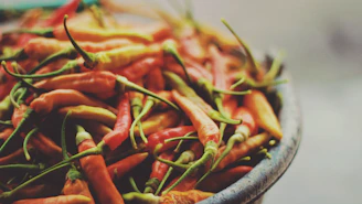 Close-up of a vibrant mix of dried chili peppers spilling from a rustic wooden bowl.