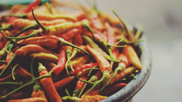 Close-up of a vibrant mix of dried chili peppers spilling from a rustic wooden bowl.