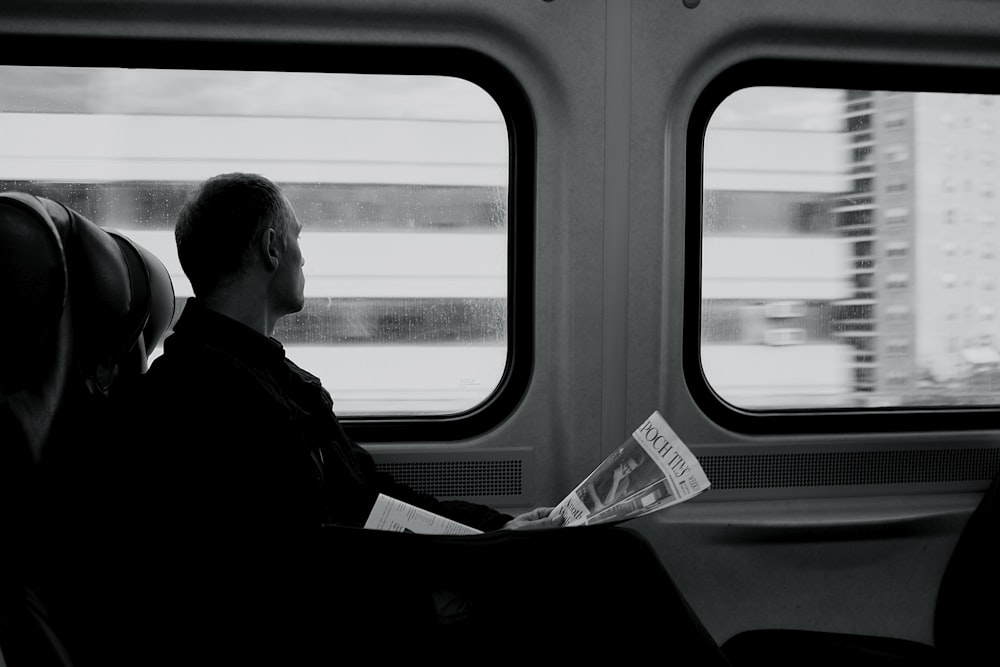 uomo all'interno del treno che guarda sul finestrino mentre tiene la fotografia in scala di grigi del giornale