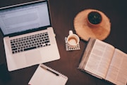A cozy workspace with a laptop, notebook, and coffee cup on a wooden table.