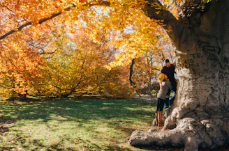 Joyful scene of Emma and Marcus reading together under a big oak tree with colorful leaves.