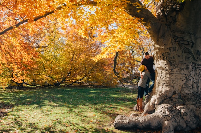 A candid shot of the couple laughing together in a sunlit forest with burnt orange leaves.