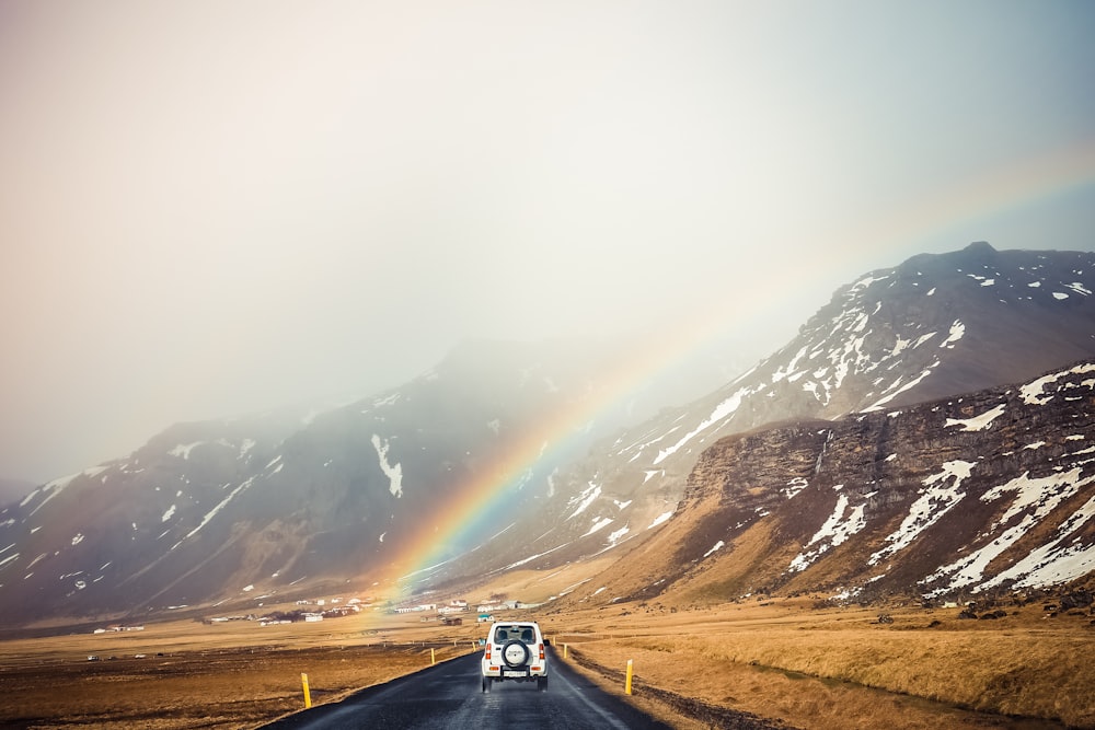 coche blanco que viaja cerca de las montañas con arco iris